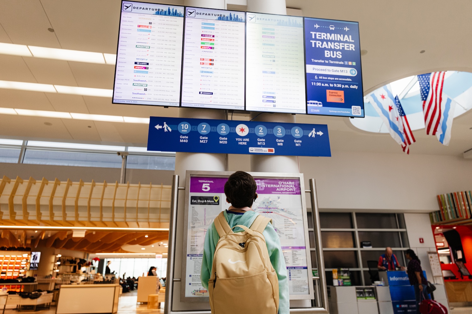 A traveler with a backpack looks at flight departure boards and gate information in O'Hare International Airport's Terminal 5.